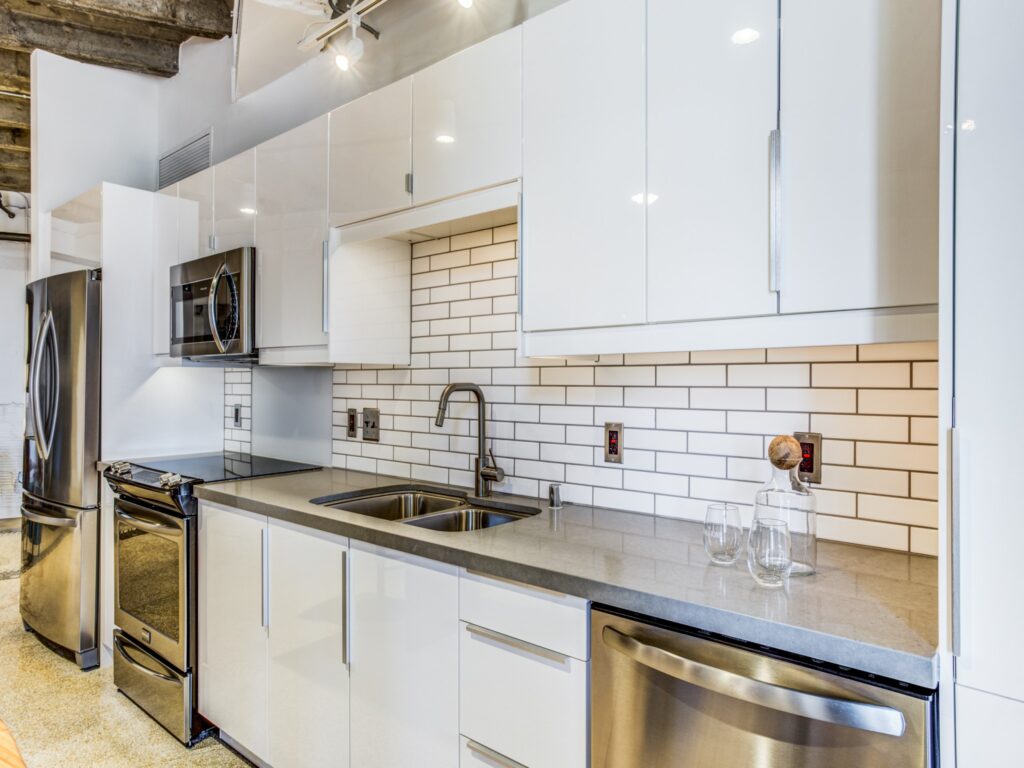 Kitchen with staineless steel appliances, gloss white cabinets, and tiled backsplash.