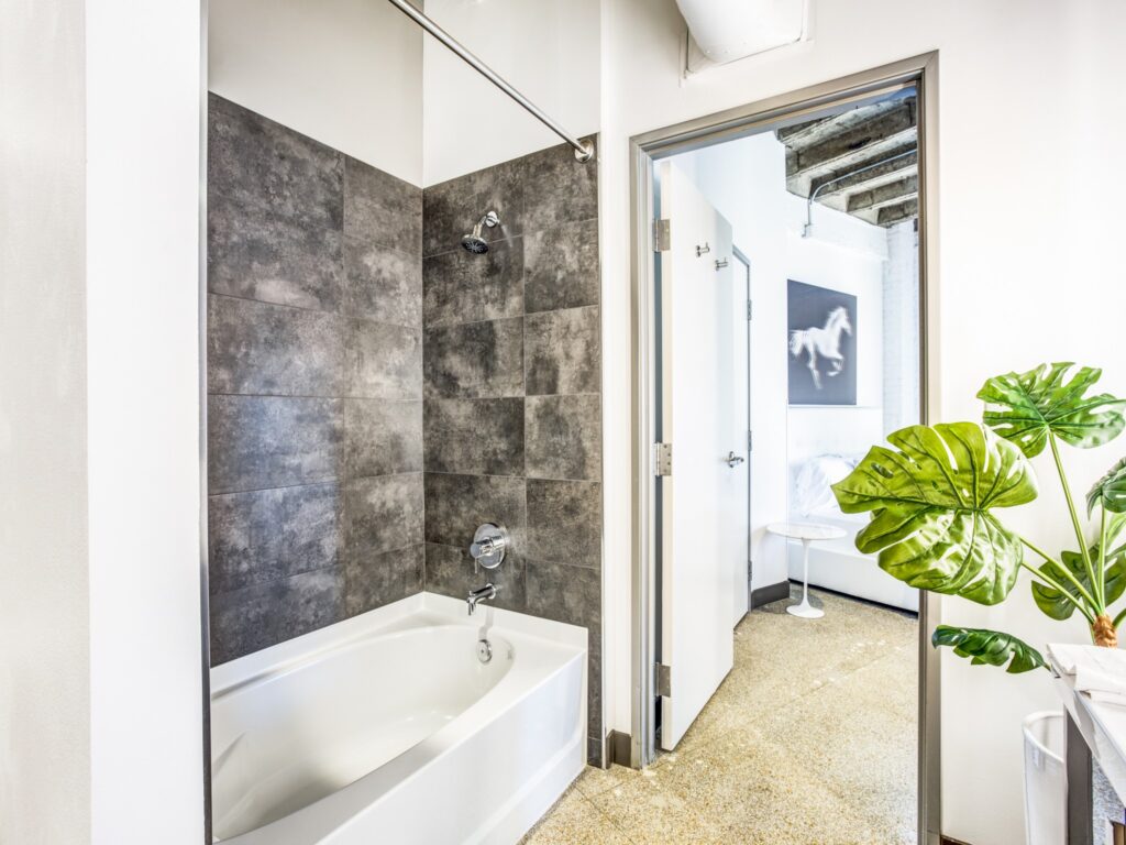 Bathroom connecting to bedroom, regular sized bath tub with granite-style tiling.