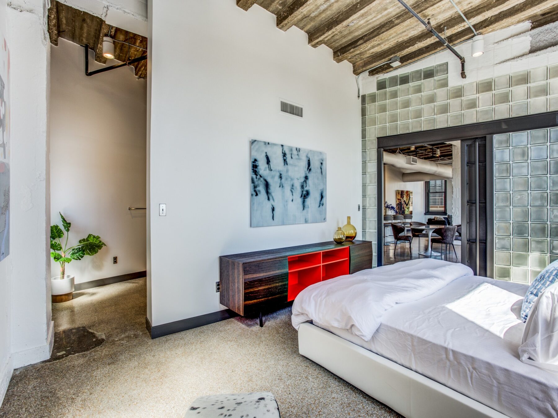 Bedroom with hard flooring, wooden rafters above bed, decorative glass wall with sliding barn door.
