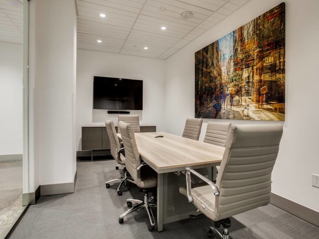 Larger conference room with long conference table, 6 rolling chairs, flat screen TV , and large bold artwork
