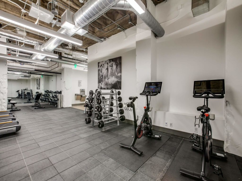 Fitness center with modern gray tile, cardio and strength equipment, water fountain, and exposed ducts, rafters and beams on ceiling