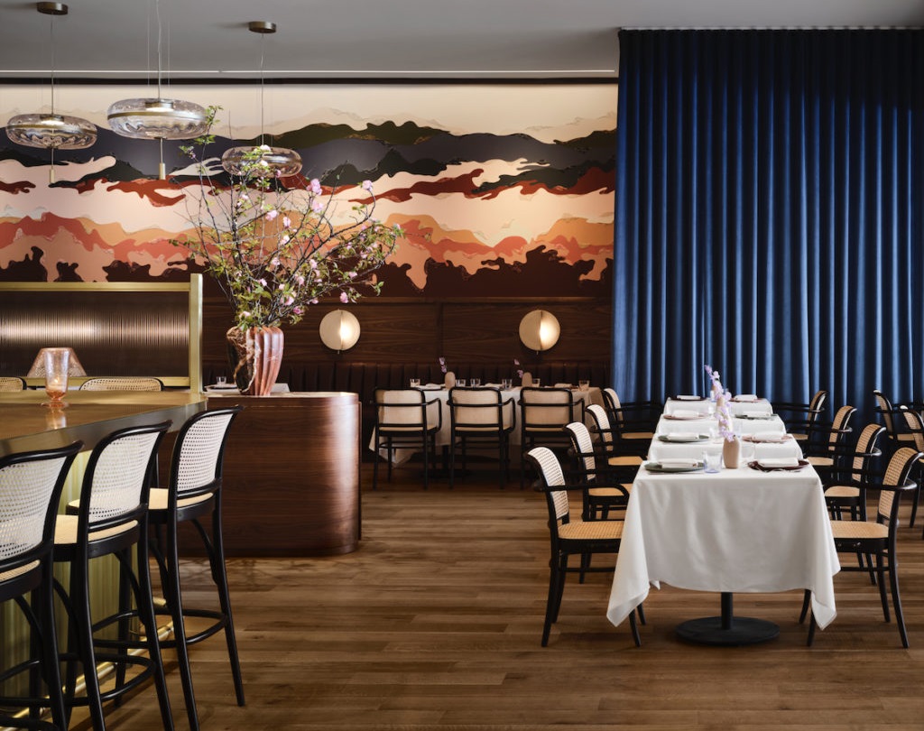 High-end restaurant with designer lighting, table seating, wall art, plant decor, and wood-style flooring