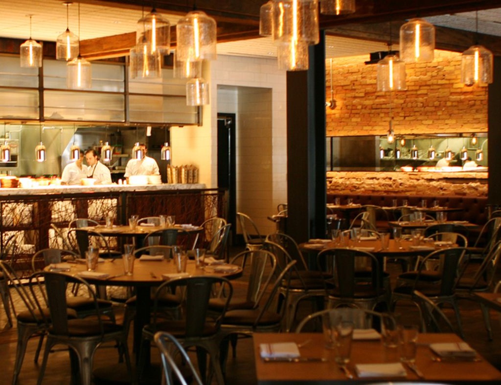 High-end restaurant with designer lighting, table seating, wall art, plant decor, and wood-style flooring